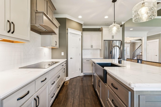 kitchen with stainless steel refrigerator, an island with sink, white cabinets, black electric cooktop, and decorative light fixtures