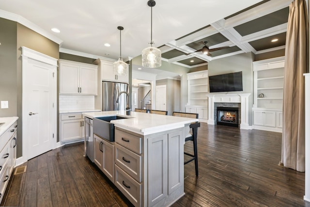 kitchen with pendant lighting, a kitchen island with sink, white cabinetry, stainless steel appliances, and coffered ceiling