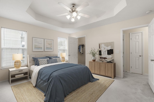 carpeted bedroom with ceiling fan, a raised ceiling, and multiple windows