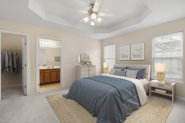 carpeted bedroom with sink, a spacious closet, a raised ceiling, ensuite bath, and a closet