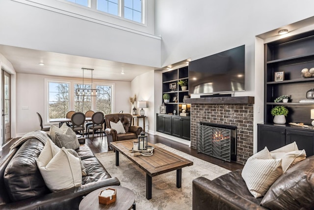 living room with a towering ceiling, a fireplace, hardwood / wood-style floors, and built in features