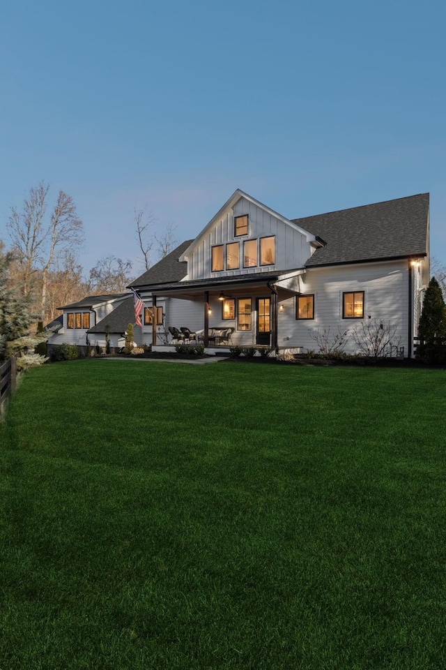 back house at dusk featuring a lawn and a patio area