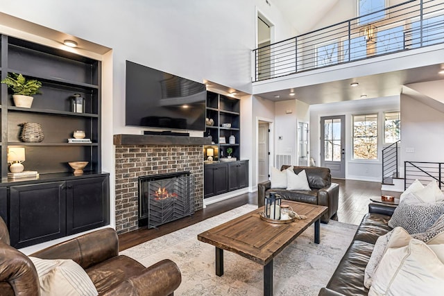 living room with a high ceiling, hardwood / wood-style floors, a fireplace, and built in shelves