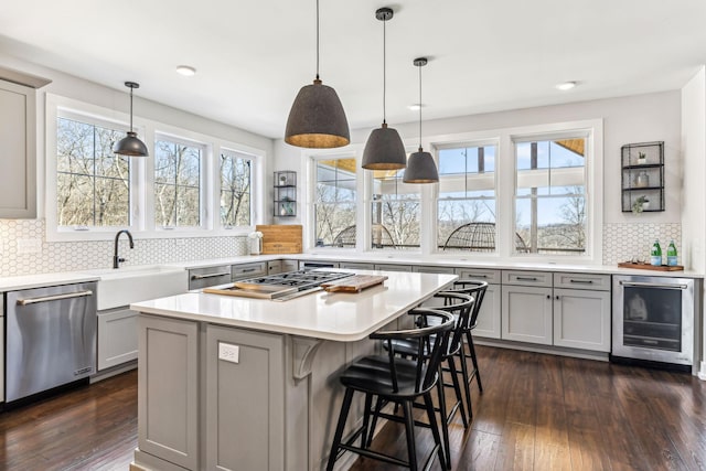 kitchen with appliances with stainless steel finishes, beverage cooler, gray cabinets, and decorative light fixtures