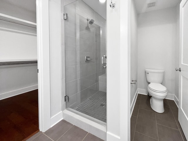 bathroom featuring tile patterned flooring, a shower with door, and toilet