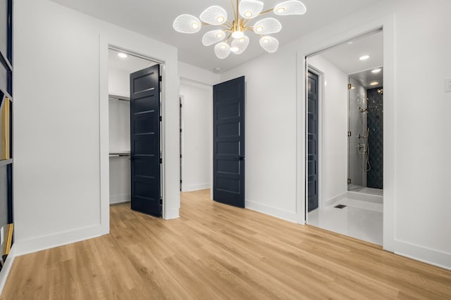 unfurnished bedroom with ensuite bath, light hardwood / wood-style flooring, a notable chandelier, a walk in closet, and a closet