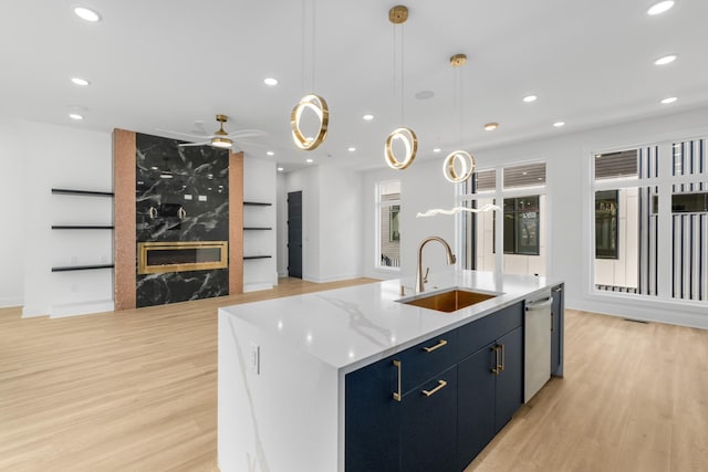 kitchen with sink, decorative light fixtures, light hardwood / wood-style flooring, stainless steel dishwasher, and a kitchen island with sink