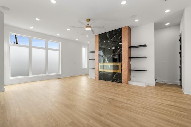 unfurnished living room featuring a premium fireplace, ceiling fan, and light hardwood / wood-style flooring