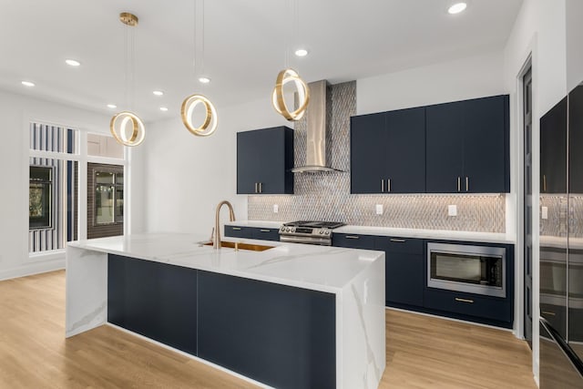 kitchen featuring decorative light fixtures, built in microwave, a kitchen island with sink, stainless steel range with gas stovetop, and wall chimney exhaust hood