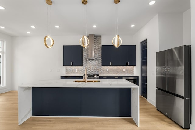 kitchen with hanging light fixtures, light stone countertops, black fridge, wall chimney exhaust hood, and light wood-type flooring