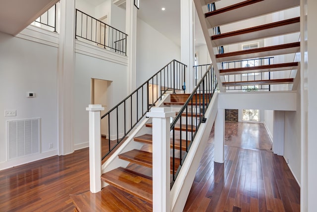 stairs with hardwood / wood-style floors and a high ceiling