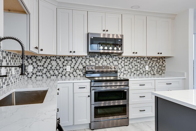 kitchen with appliances with stainless steel finishes, tasteful backsplash, white cabinetry, sink, and light stone countertops