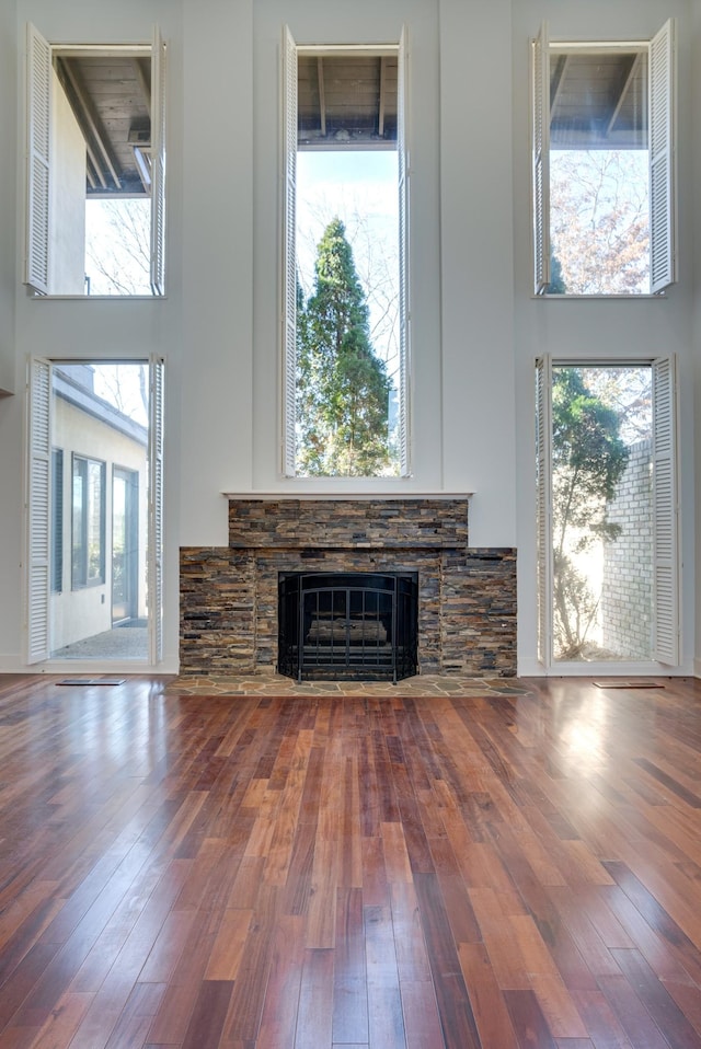 unfurnished living room with a stone fireplace, a towering ceiling, and hardwood / wood-style floors