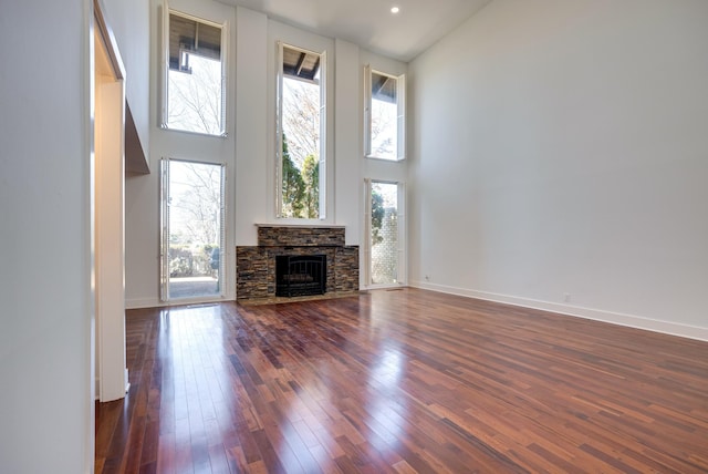 unfurnished living room featuring a towering ceiling, a stone fireplace, dark hardwood / wood-style floors, and a wealth of natural light