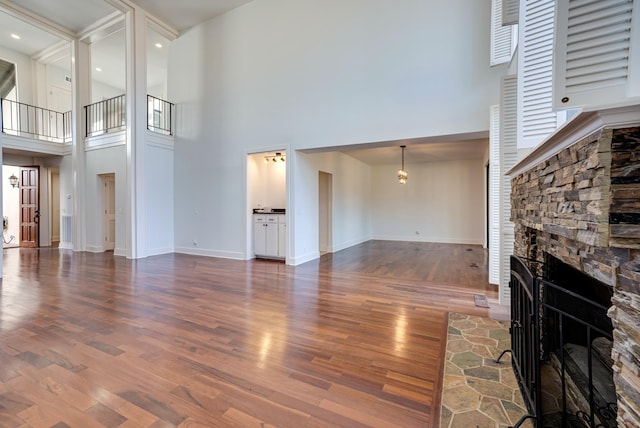 living room with a high ceiling, a stone fireplace, and dark wood-type flooring