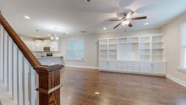 unfurnished living room featuring ceiling fan with notable chandelier and dark hardwood / wood-style flooring