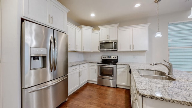 kitchen featuring sink, stainless steel appliances, light stone countertops, white cabinets, and decorative light fixtures