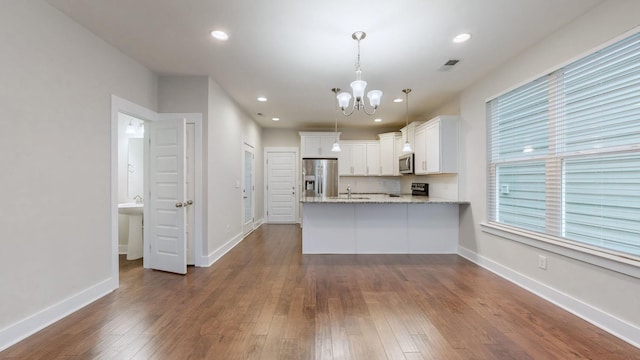 kitchen featuring appliances with stainless steel finishes, dark hardwood / wood-style floors, decorative light fixtures, white cabinets, and kitchen peninsula