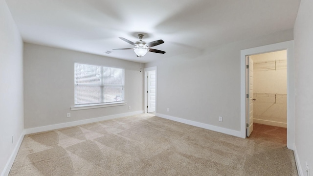 unfurnished bedroom featuring ceiling fan, a spacious closet, a closet, and light carpet