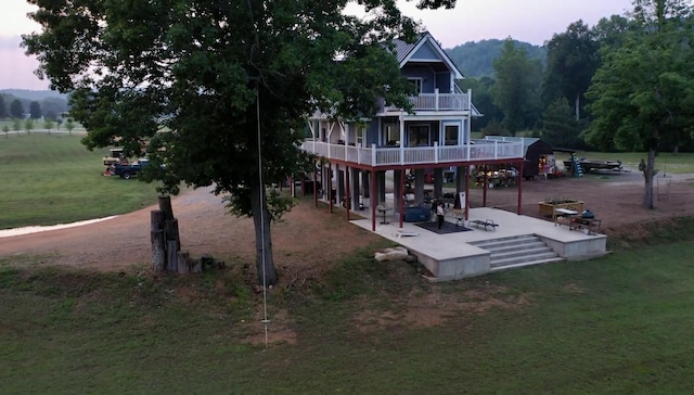 back house at dusk with a balcony, a yard, and a patio