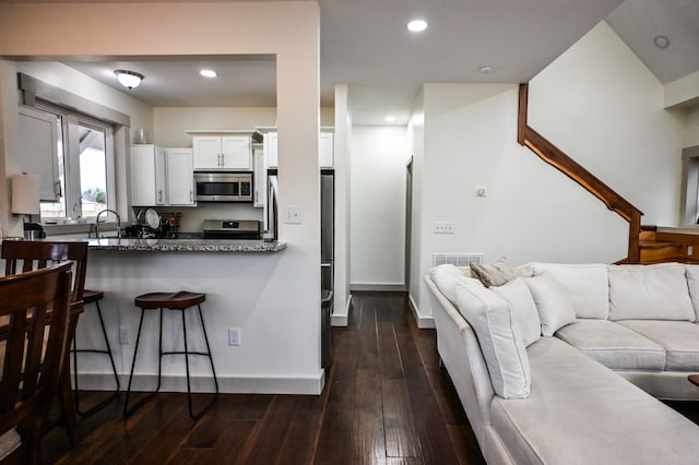 kitchen featuring appliances with stainless steel finishes, dark hardwood / wood-style floors, white cabinetry, sink, and dark stone counters