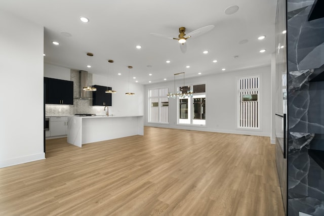 unfurnished living room with sink, ceiling fan with notable chandelier, and light hardwood / wood-style floors