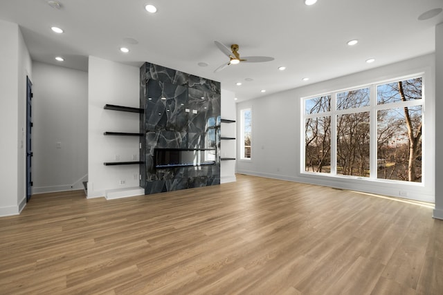 unfurnished living room with ceiling fan, a premium fireplace, and light hardwood / wood-style flooring