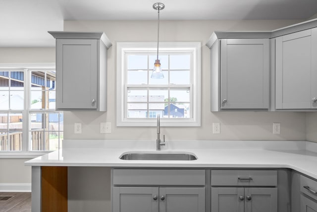 kitchen with hanging light fixtures, hardwood / wood-style flooring, sink, and gray cabinetry