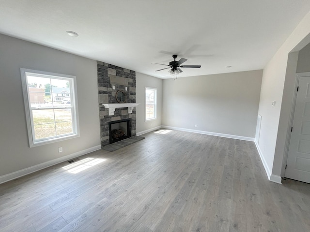 unfurnished living room with ceiling fan, a stone fireplace, light hardwood / wood-style floors, and a wealth of natural light