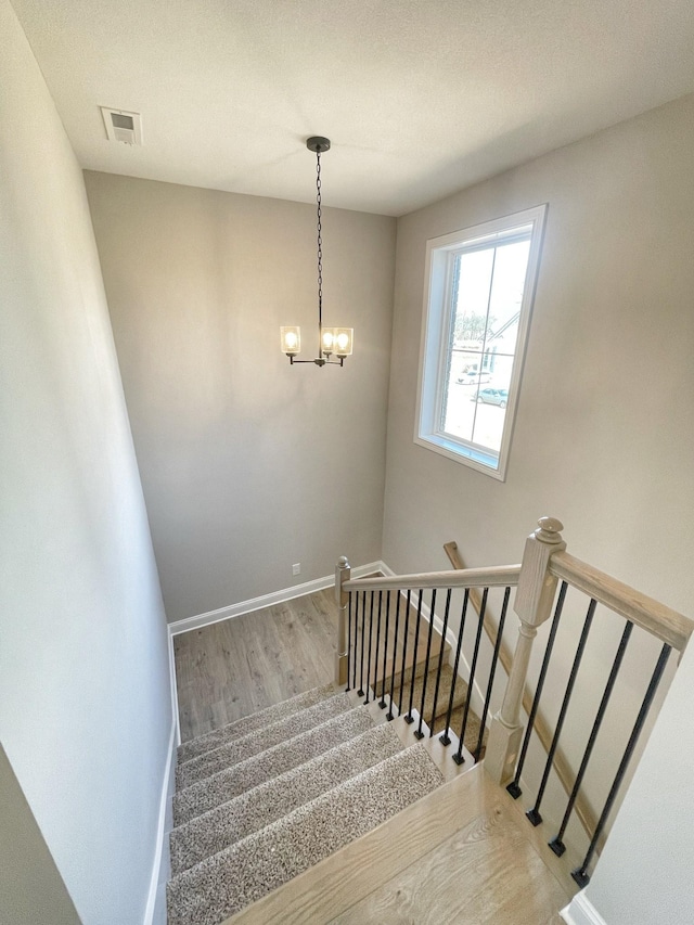 stairs with wood-type flooring and a chandelier