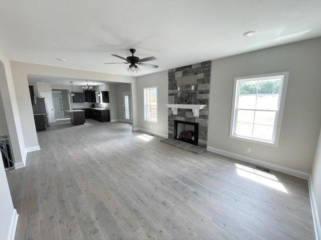 unfurnished living room with a stone fireplace, a wealth of natural light, light hardwood / wood-style floors, and ceiling fan