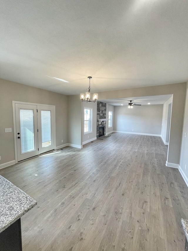 unfurnished living room featuring a stone fireplace, ceiling fan with notable chandelier, a textured ceiling, and light wood-type flooring