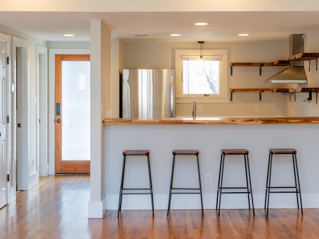 kitchen with recessed lighting, wood finished floors, a breakfast bar area, and freestanding refrigerator