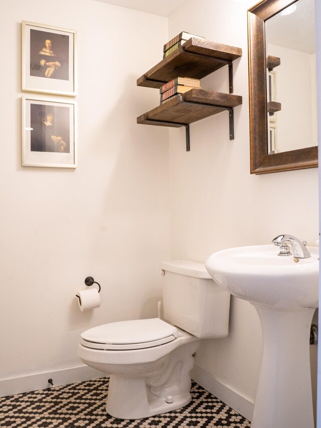 half bath featuring toilet, baseboards, and a sink