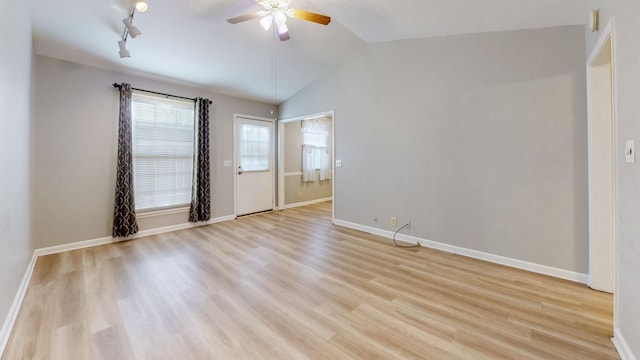 empty room featuring ceiling fan, rail lighting, vaulted ceiling, and light hardwood / wood-style flooring