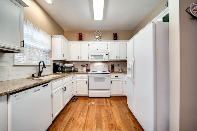 kitchen with white cabinetry, sink, light stone counters, and white appliances