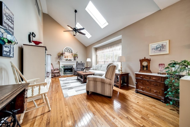 living room featuring ceiling fan, high vaulted ceiling, light wood-type flooring, and a skylight