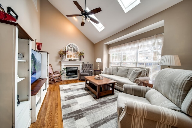 living room with ceiling fan, high vaulted ceiling, light hardwood / wood-style floors, and a skylight