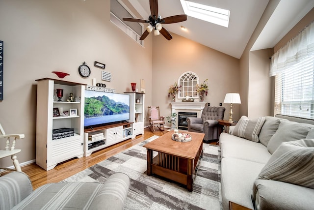 living room featuring light hardwood / wood-style flooring, a skylight, high vaulted ceiling, and ceiling fan