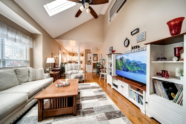 living room featuring ceiling fan, hardwood / wood-style floors, a skylight, high vaulted ceiling, and ornate columns