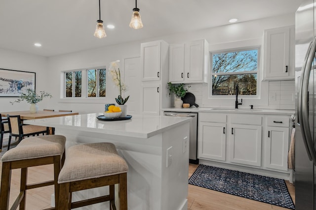 kitchen with pendant lighting, sink, white cabinetry, stainless steel appliances, and a center island