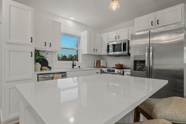 kitchen with appliances with stainless steel finishes, sink, a breakfast bar area, white cabinets, and hanging light fixtures