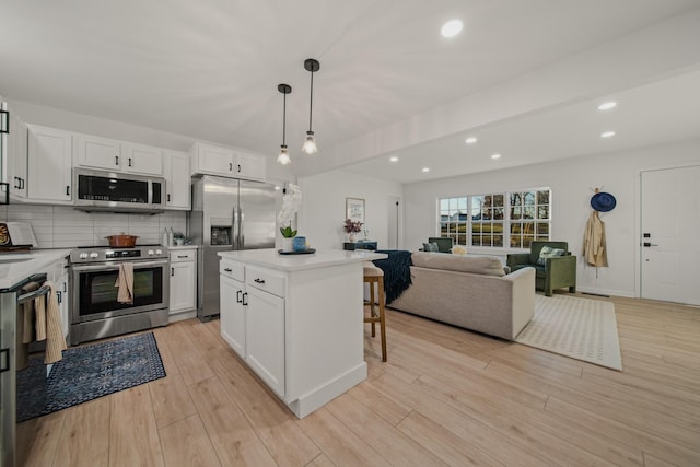 kitchen with a breakfast bar area, appliances with stainless steel finishes, a kitchen island, pendant lighting, and white cabinets