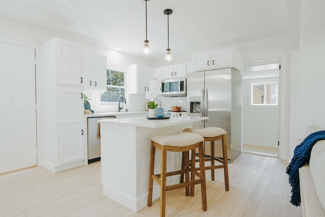 kitchen with white cabinetry, hanging light fixtures, a kitchen island, stainless steel appliances, and backsplash