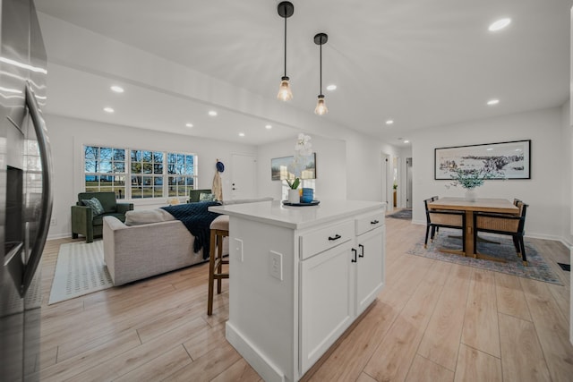 kitchen with white cabinetry, hanging light fixtures, light hardwood / wood-style flooring, and a kitchen island