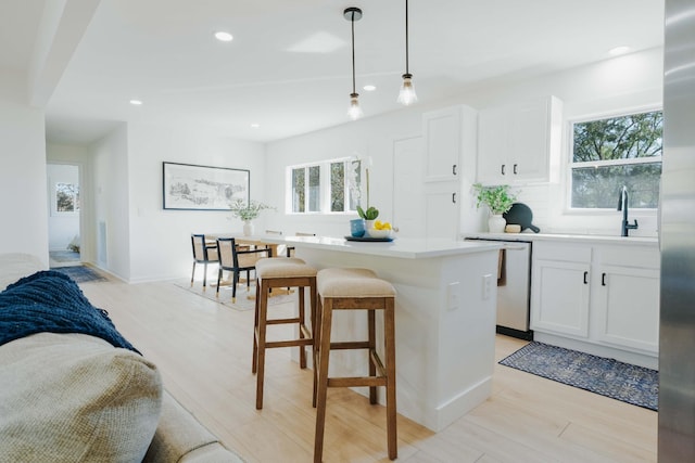 kitchen with decorative light fixtures, white cabinetry, sink, a center island, and stainless steel dishwasher