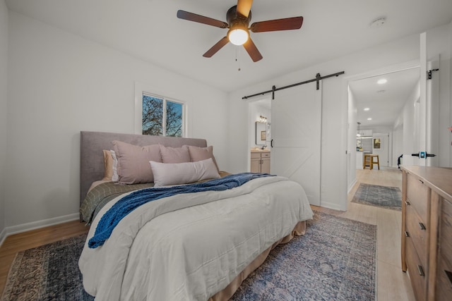 bedroom featuring ceiling fan, a barn door, light hardwood / wood-style floors, and ensuite bath