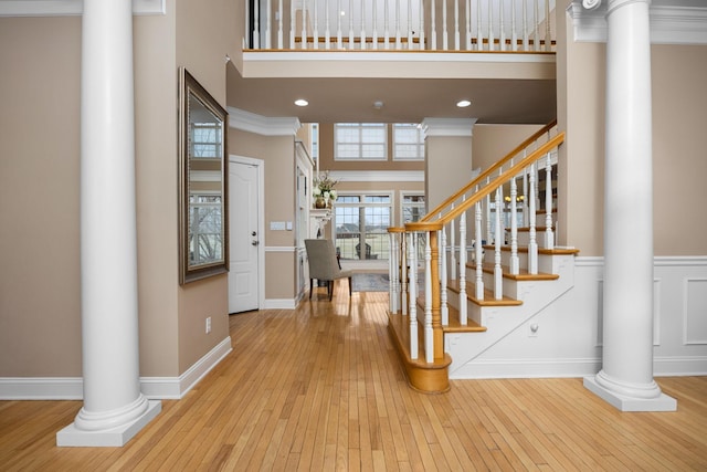 entryway with crown molding, decorative columns, a high ceiling, and light wood-type flooring