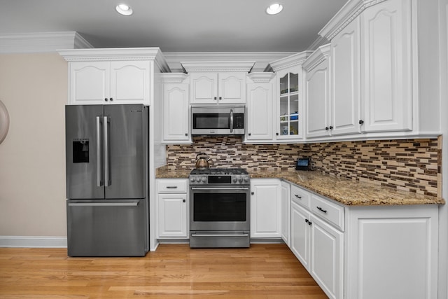 kitchen with white cabinetry, stainless steel appliances, ornamental molding, decorative backsplash, and dark stone counters