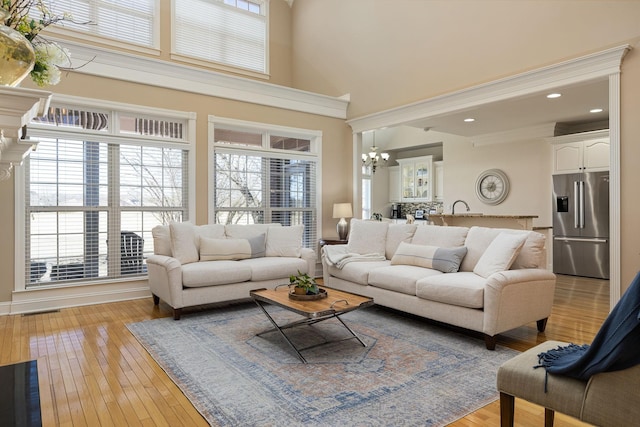 living room with sink, light wood-type flooring, ornamental molding, a notable chandelier, and a high ceiling